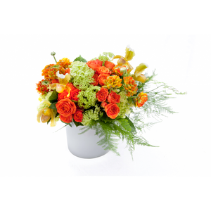 Flower arrangement in a low, round, white, ceramic vase, green viburnum, orange spray roses, orange ranunculus, yellow orchids and asparagus fern
