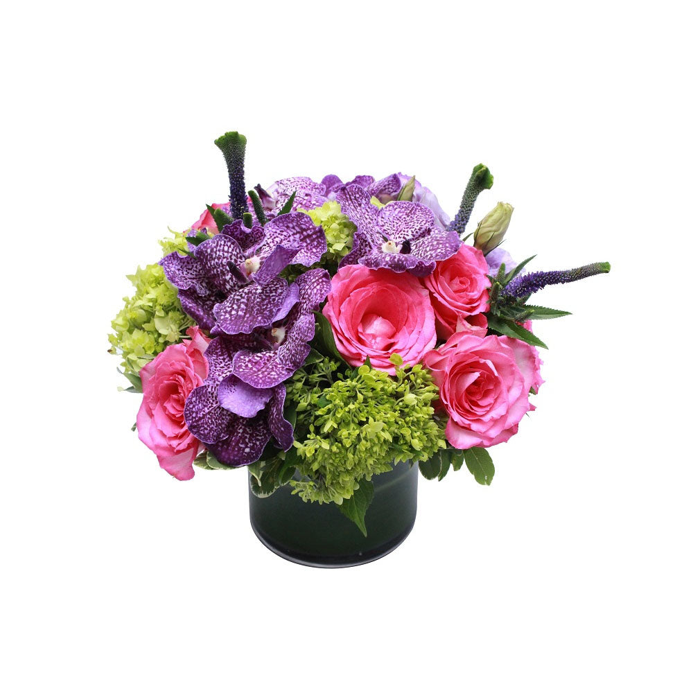 Flower arrangement in a low, round, black, ceramic vase, pink roses, purple vanda orchids, green hydrangeas and blue veronicas