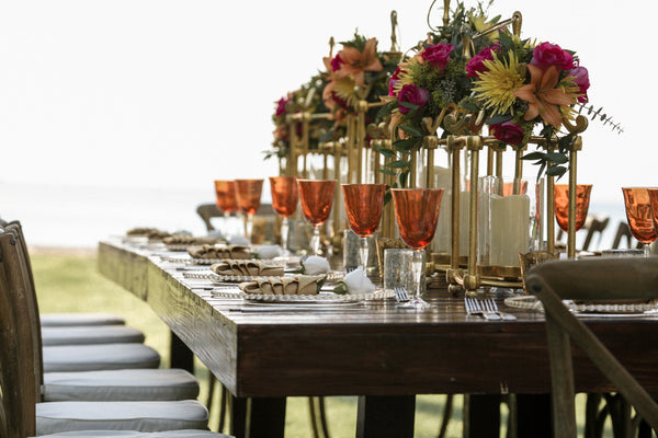 Dark wood table outside during a wedding featuring flower arrangement centerpieces and full dining sets 