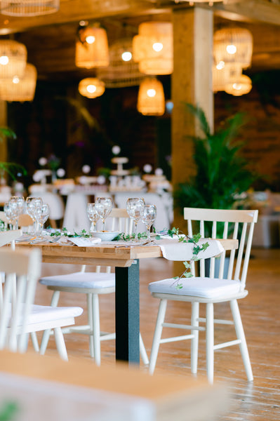 Table and chairs with decorative flower centerpieces at an event with lanterns overhead in a rustic hall