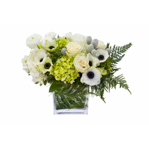 Flower arrangement in a low, square, clear glass vase, green hydrangea, white hydrangeas, white roses, white anemones, white ranunculus, leather leaves and silver pinecones