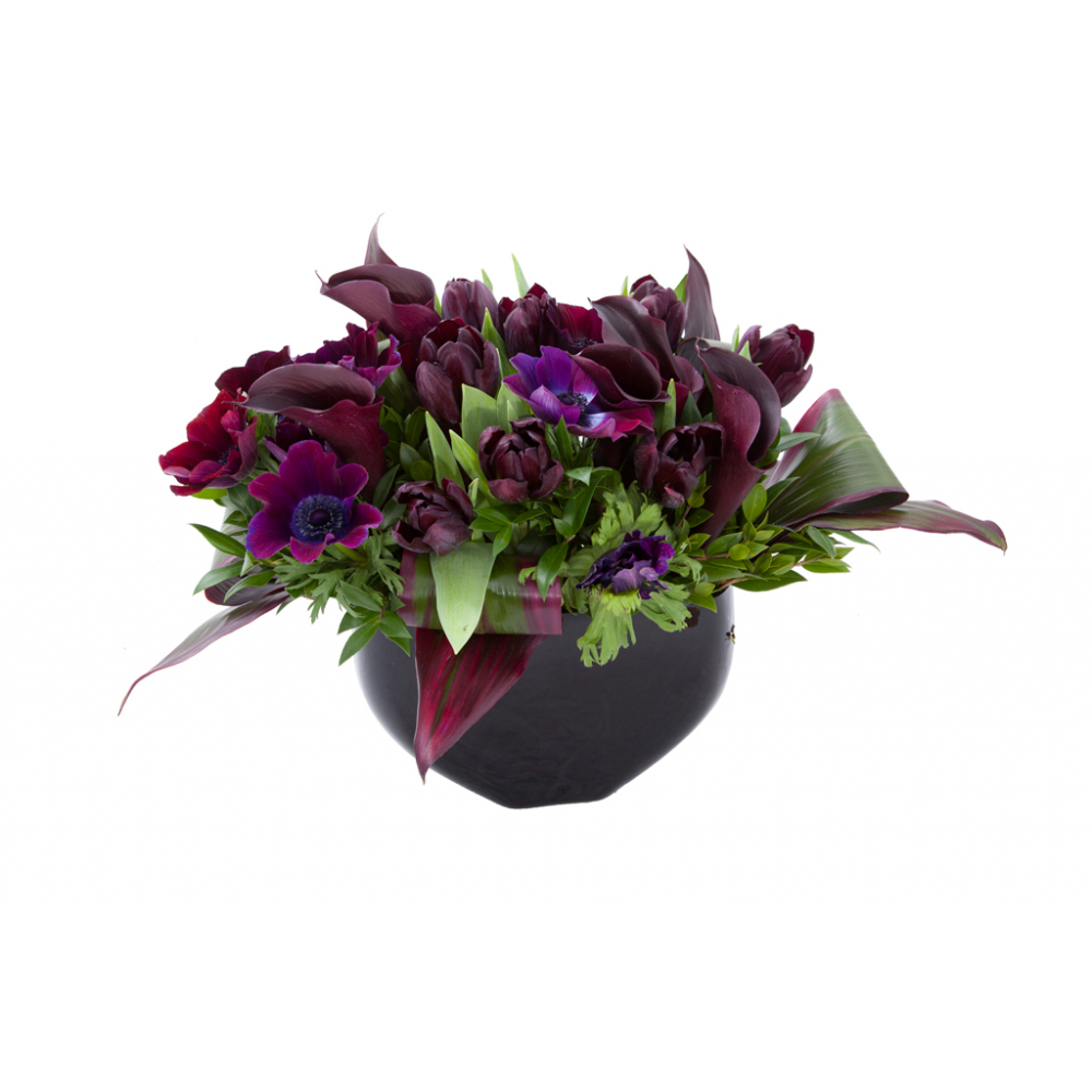 Flower arrangement in a low, round, black ceramic vase, black calla lilies, deep purple anemones and tulips