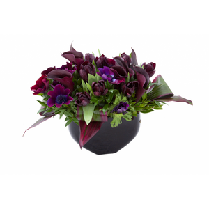 Flower arrangement in a low, round, black ceramic vase, black calla lilies, deep purple anemones and tulips