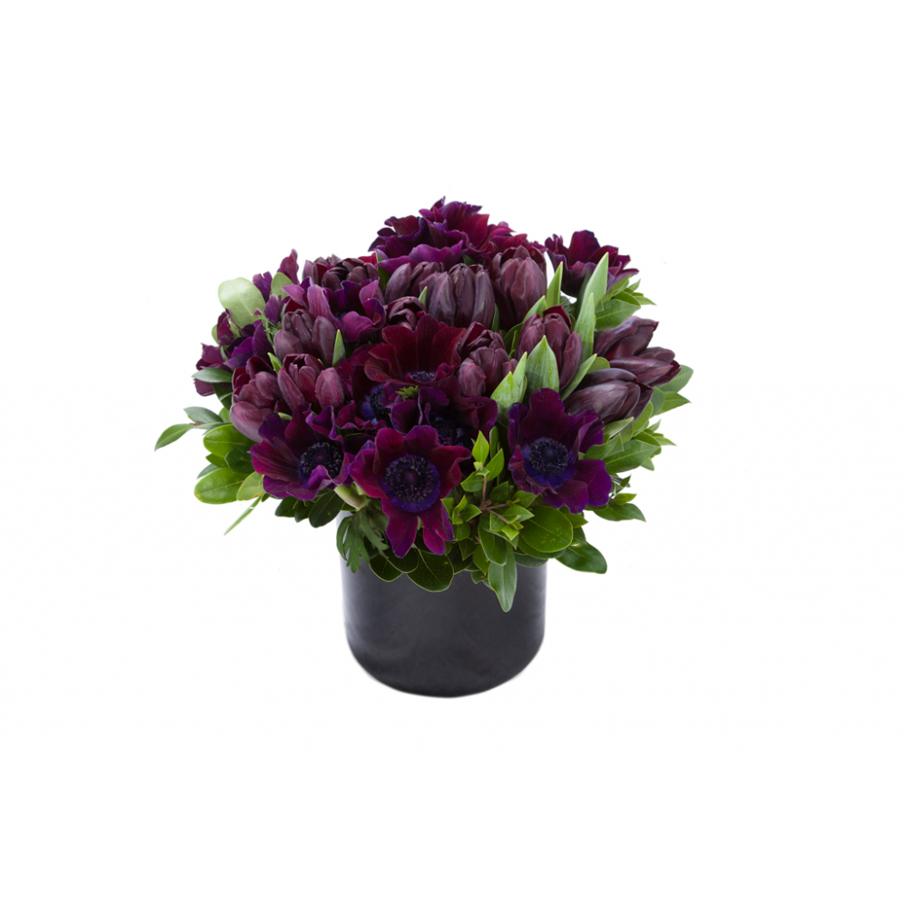 Flower arrangement in a low, round, black ceramic vase, deep purple anemones and tulips