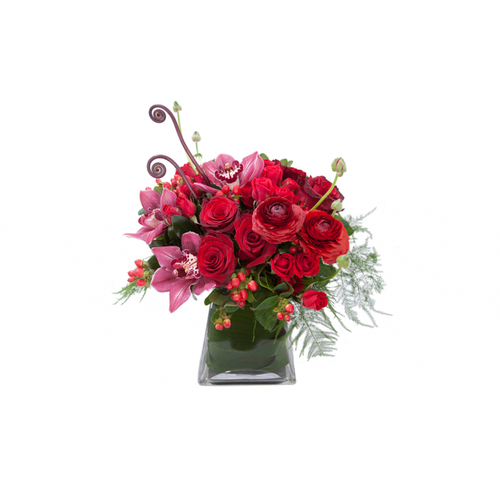 Flower arrangement in a medium tall, square, tapered vase, red roses, red spray roses, red ranunculus, red hypericum and red cymbidium orchids