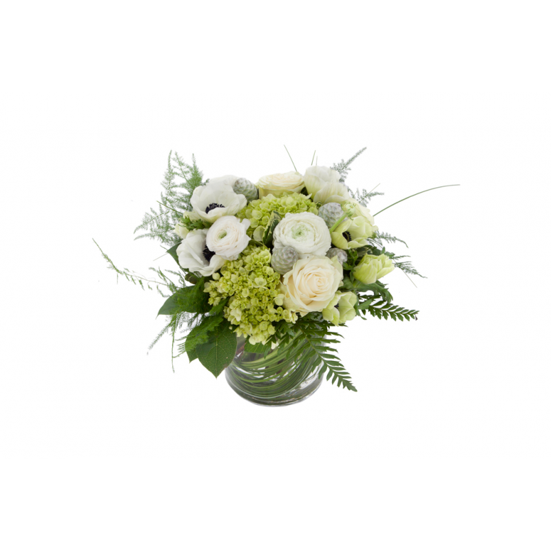 Flower arrangement in a low, round, clear glass vase, green hydrangea, white anemones, white roses, white ranunculus, pinecones and leather leaves.