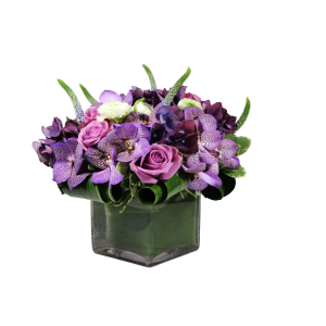 Flower arrangement in a low, square, clear glass vase, lavender roses, purple vanda orchids, purple hydrangea and blue veronica.