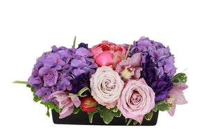 Flower arrangement in a low, rectangle, black ceramic vase, purple hydrangeas, coral peonies, pink cymbidium orchids and purple lisianthus