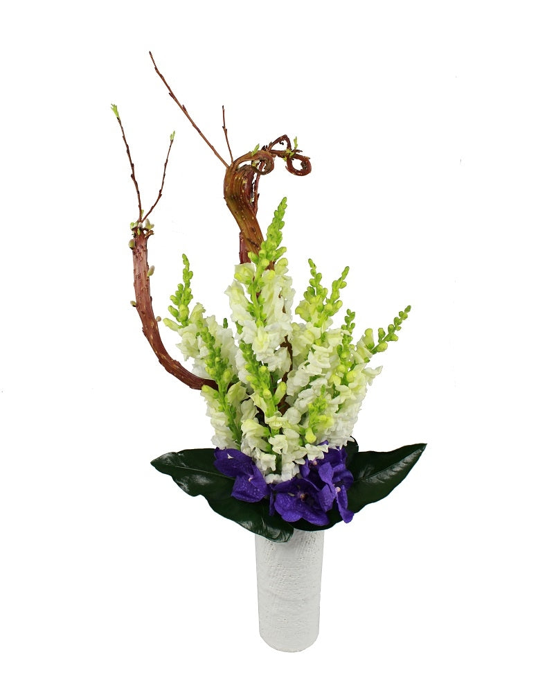 Flower arrangement in a tall, round, white, ceramic vase, tall branches, white snapdragons, exotic leaves and purple vanda orchids