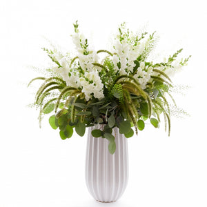 Flower arrangement in a tall, round, white, ceramic vase, white snapdragons, grass, and silver dollar eucalyptus