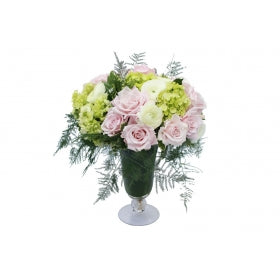 Flower arrangement in a low, tulip shape, clear glass vase, pink spray roses, green hydrangeas, white ranunculus and asparagus fern