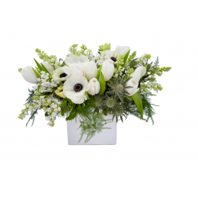 Flower arrangement in a low, white ceramic vase, white lilac, white anemones, white tulips, green thistle