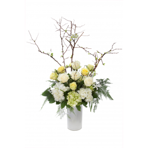 Flower arrangement in a tall, round, white glass vase, white flowering branches, white and green hydrangeas, white and green roses and asparagus ferns