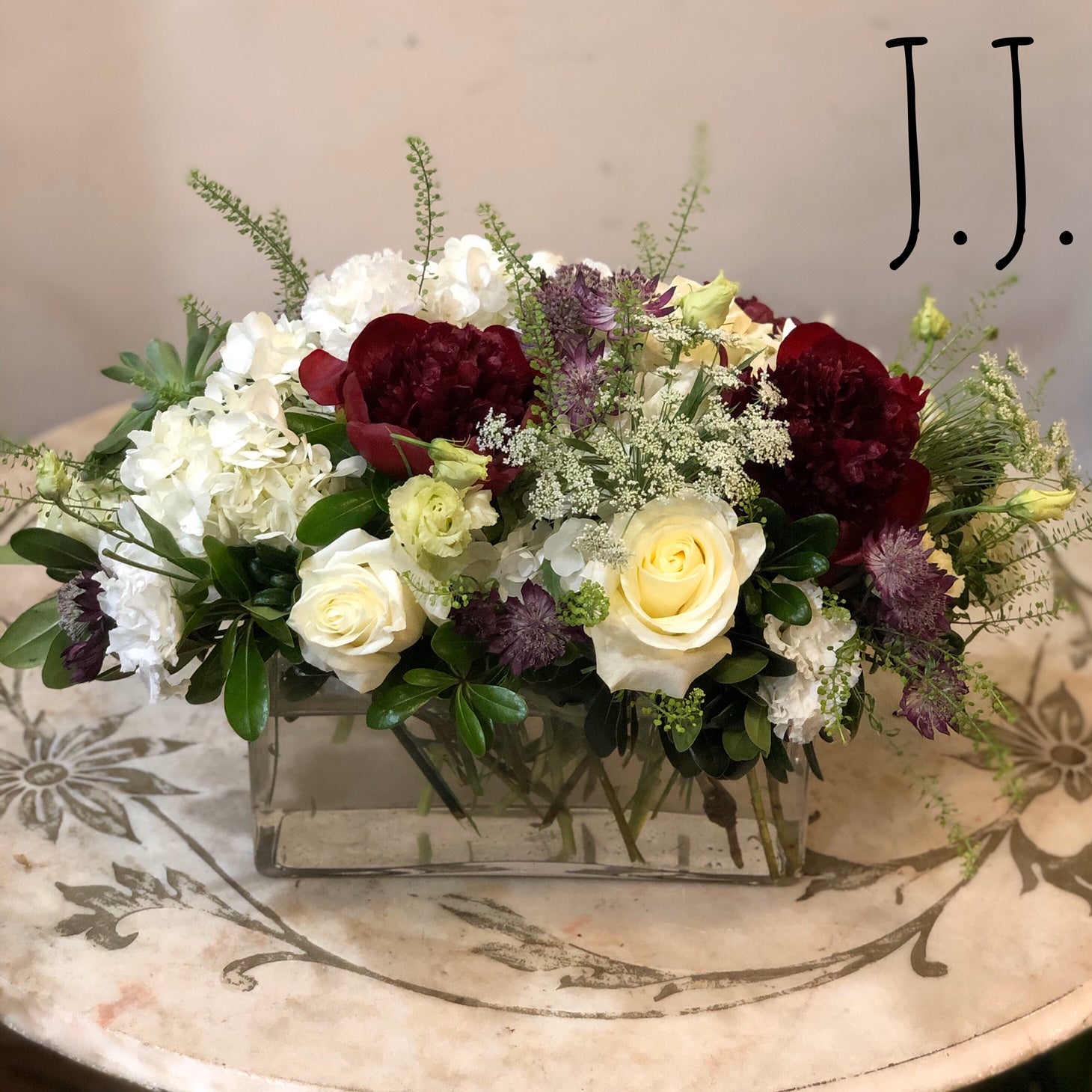 Flower arrangement in a low, rectangles, clear vase, white hydrangea, white roses, white lisianthus, red peonies and purple astrantia