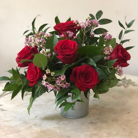 Flower arrangement in a low, zinc bucket, half dozen roses, pink wax flowers and lush greenery